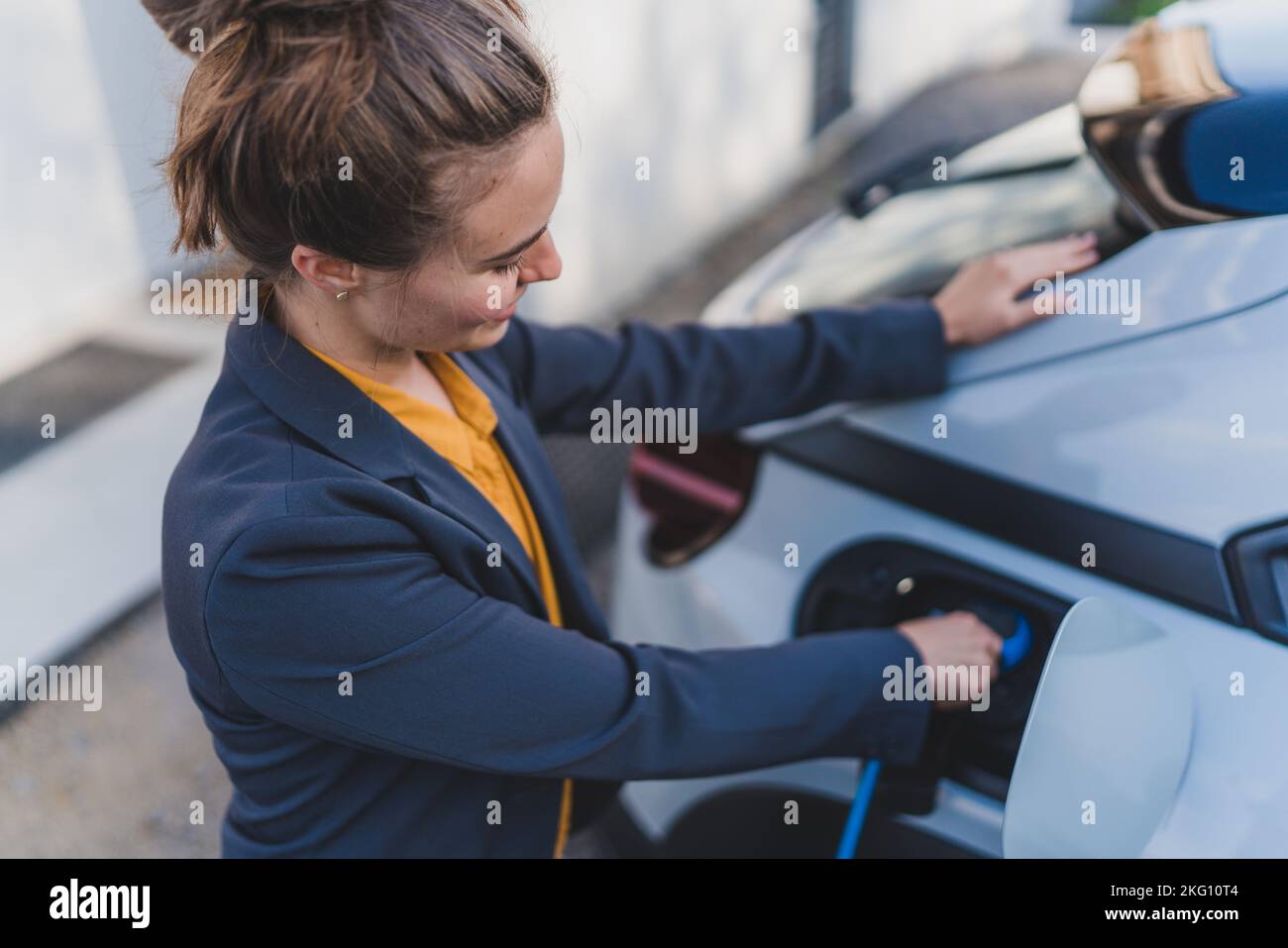 Junge Frau lädt ihr Elektroauto im nachhaltigen und wirtschaftlichen Transportkonzept zu Hause. Stockfoto