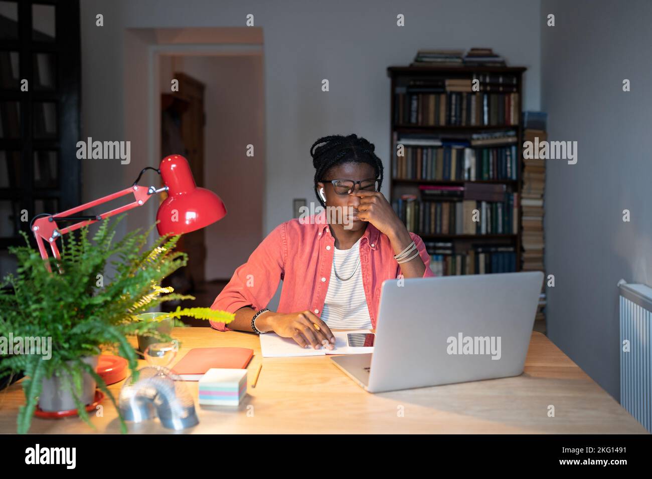 Müde gelangweilter afroamerikanischer Mann, der nach langer Arbeit am Laptop die Augen reibt, sitzt am Bürotisch Stockfoto
