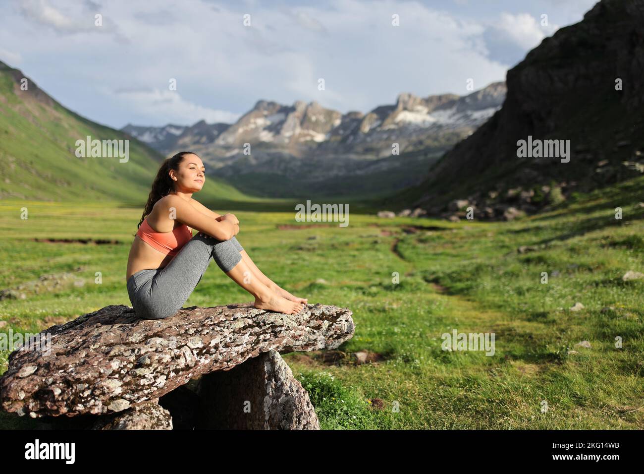 Sportlerin, die sich auf einem Dolmen ausruht und die Aussicht auf den Berg betrachtet Stockfoto