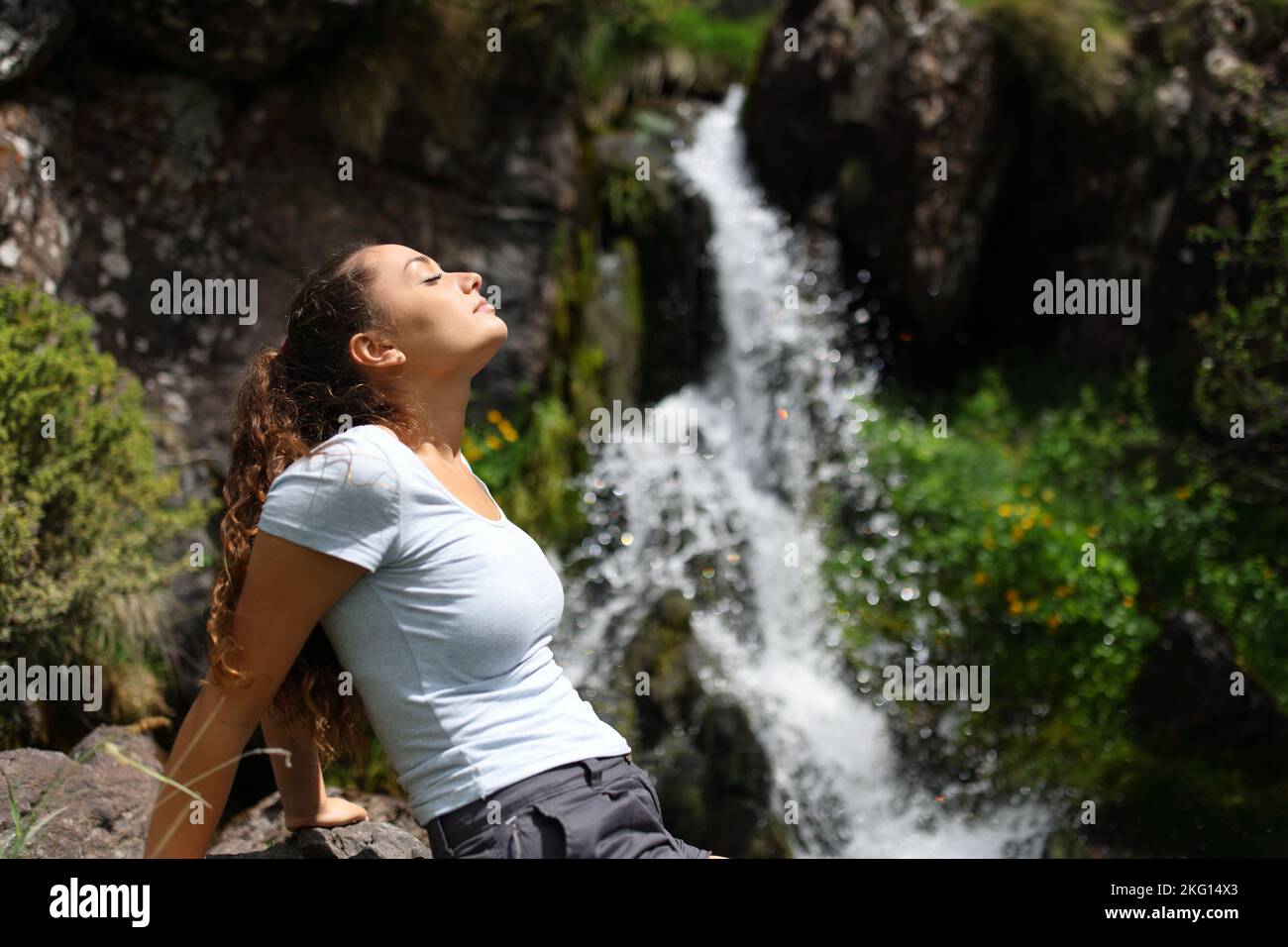 Profil einer Frau, die sich entspannt und frische Luft in einem kleinen Wasserfall atmet Stockfoto