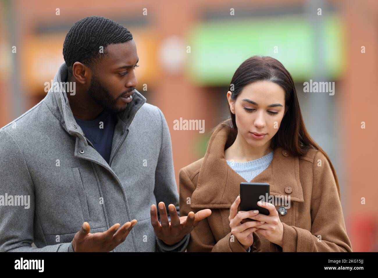 Eine Frau, die im Winter ihr Smartphone benutzt und ihren Freund auf der Straße ignoriert Stockfoto