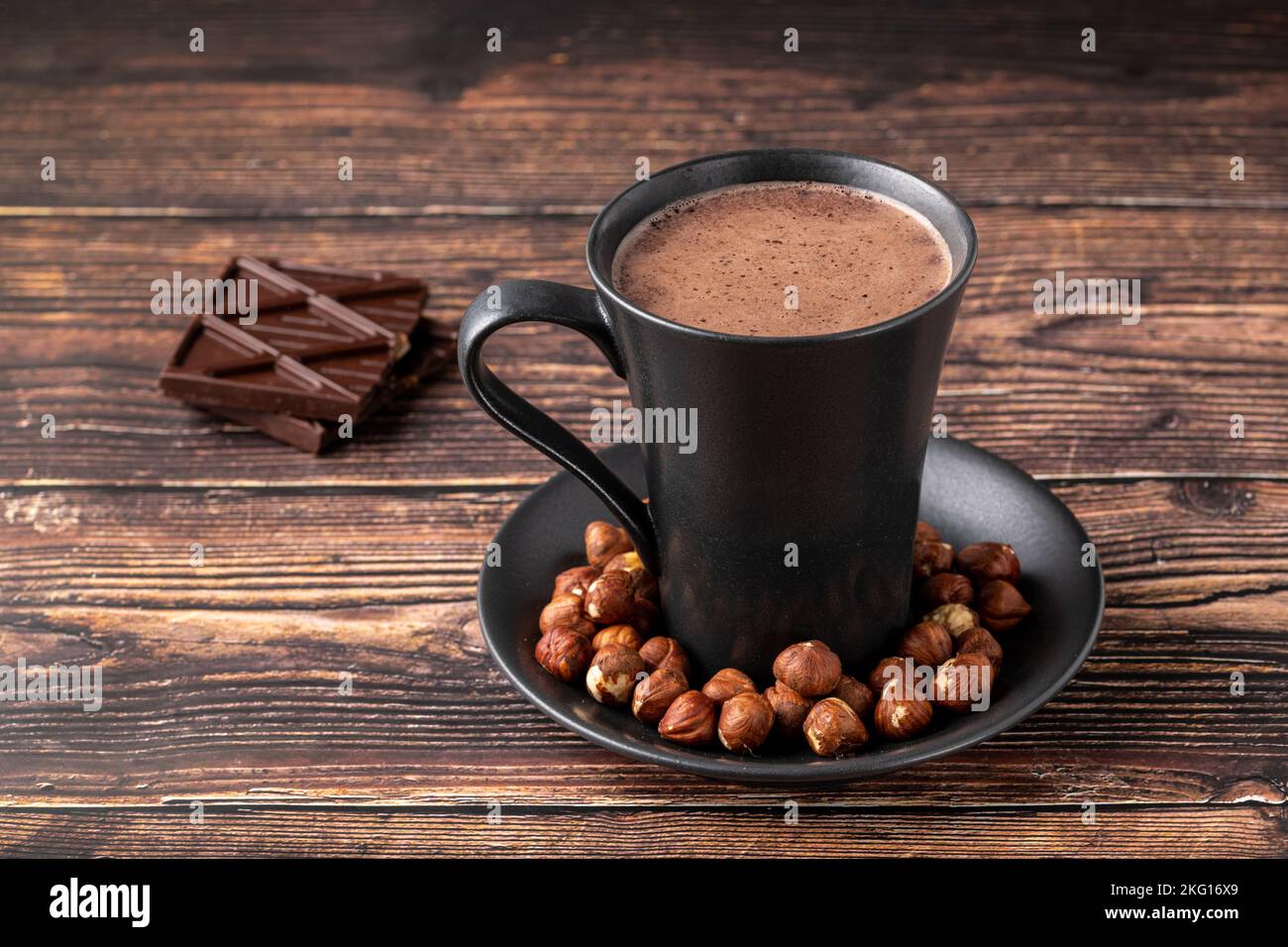 Heiße Haselnuss-Schokolade mit Schokolade daneben auf Holztisch Stockfoto