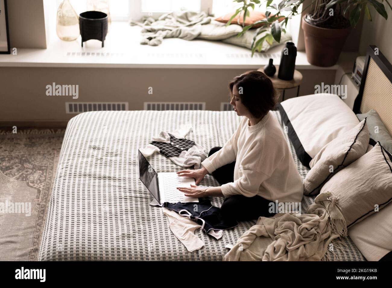 Eine Schwangere in einem warmen Pullover sitzt auf dem Bett und kauft über eine Online-Website Dinge für das Baby.das Konzept von E-Commerce, Holiday Shopping, Geschenkeinkauf für die Geburt eines Babys. Stockfoto