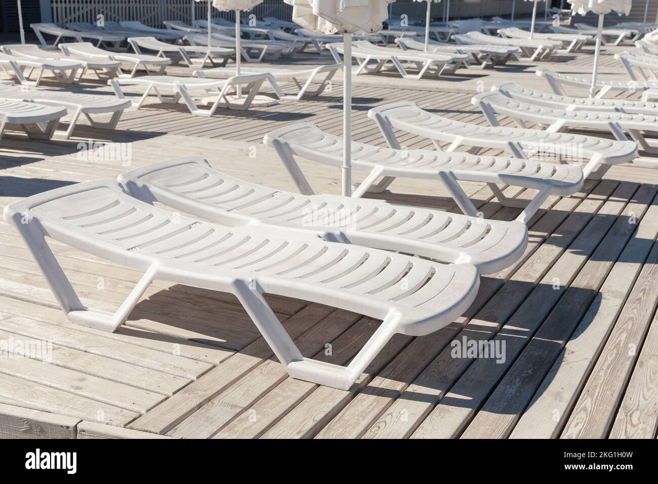 Leere weiße Sonnenliegen stehen an einem sonnigen Tag auf einer Holzterrasse Stockfoto