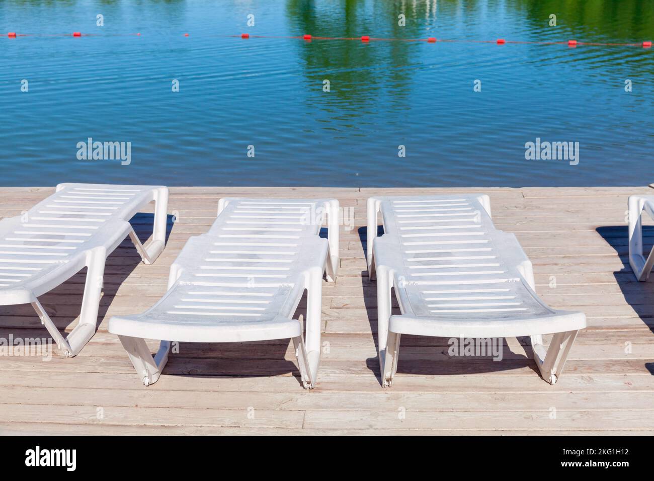 Leere weiße Sonnenliegen stehen auf einem hölzernen Pier an der Seeufer Stockfoto