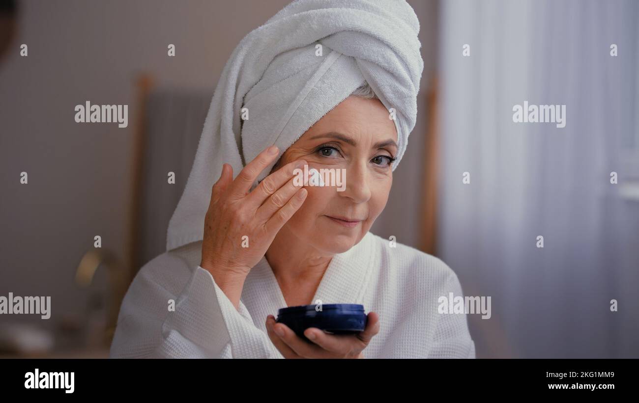 Portrait schöne kaukasische alte 60s Frau 50s Dame Großmutter im Alter von Modell mit Handtuch auf dem Kopf Gesichtspflege Gesichtslifting Hydratation gilt feuchtigkeitsspendend Stockfoto