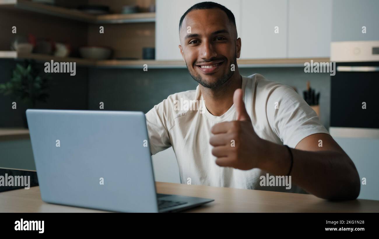 Lächelnder männlicher Sieger glücklich erfolgreicher afrikanischer Millennial Mann Kerl amerikanischer Benutzer Freiberufler zu Hause Küche Arbeit mit Laptop zufrieden mit Computer-App Stockfoto