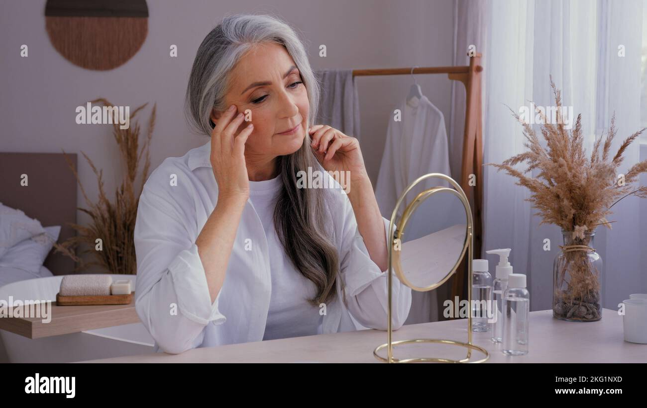 Kaukasische 60s-jährige ältere Dame alt grauhaarige 50s Frau weiblich Blick auf Spiegelreflexion Verwöhnung berühren faltigen Gesicht Anti-Aging Stockfoto