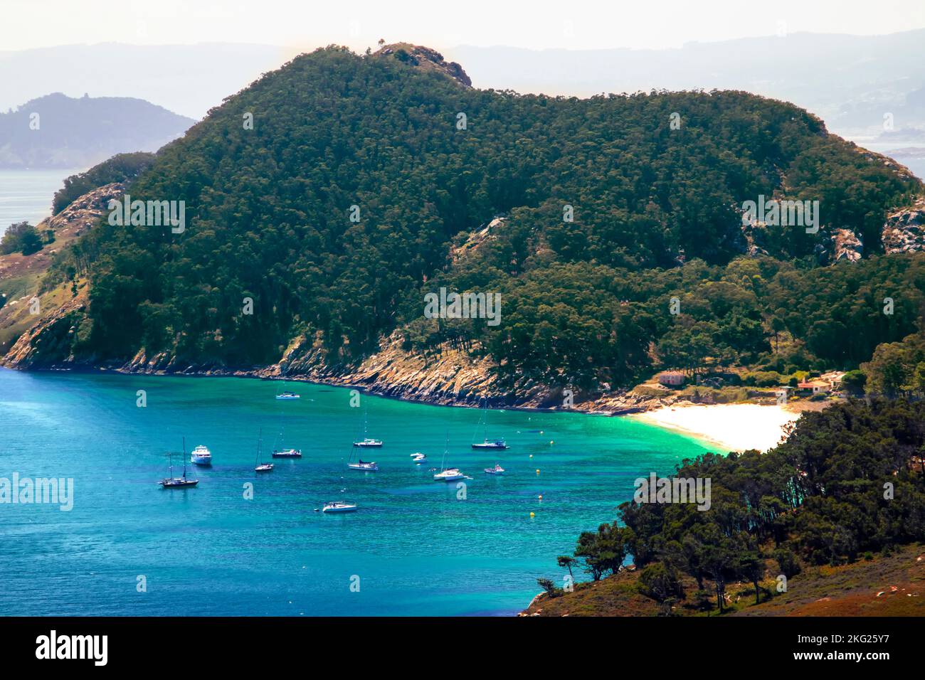 Versteckter Strand, umgeben von bewaldeten Hügeln auf den Cies-Inseln, Spanien. Türkisfarbenes Wasser mit kleinen Booten in der Nähe des Ufers Stockfoto