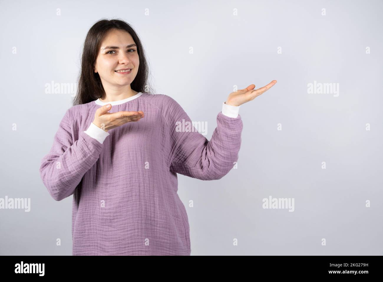 Schöne Brünette Frau in komfortablen Musselin Pyjamas von Lavendel Farbe zeigt ihre Hände an den Ort für Text Stockfoto