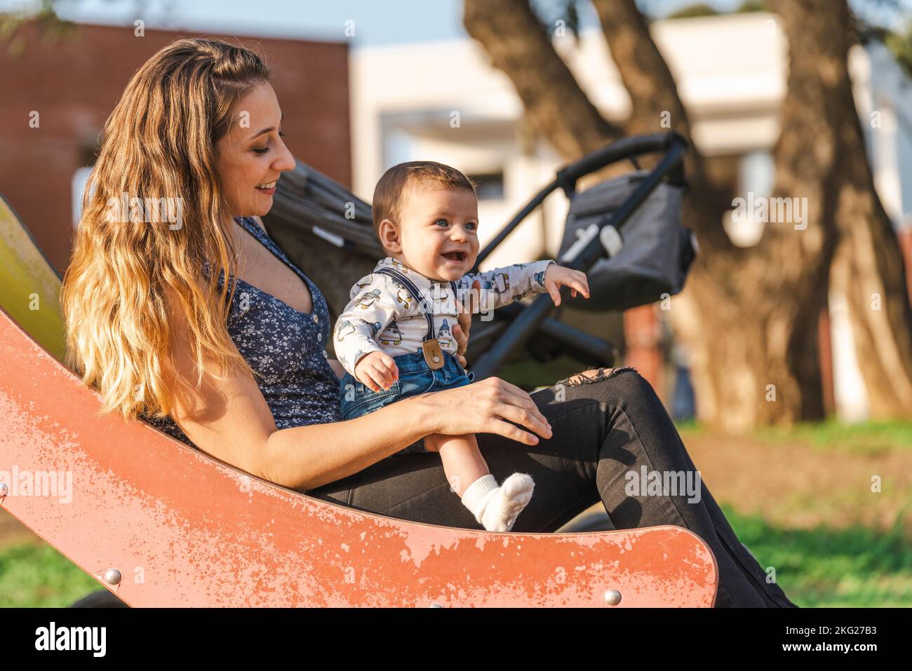 Mutter mit ihrem Baby auf einer Parkrutsche, als die Sonne untergeht Stockfoto