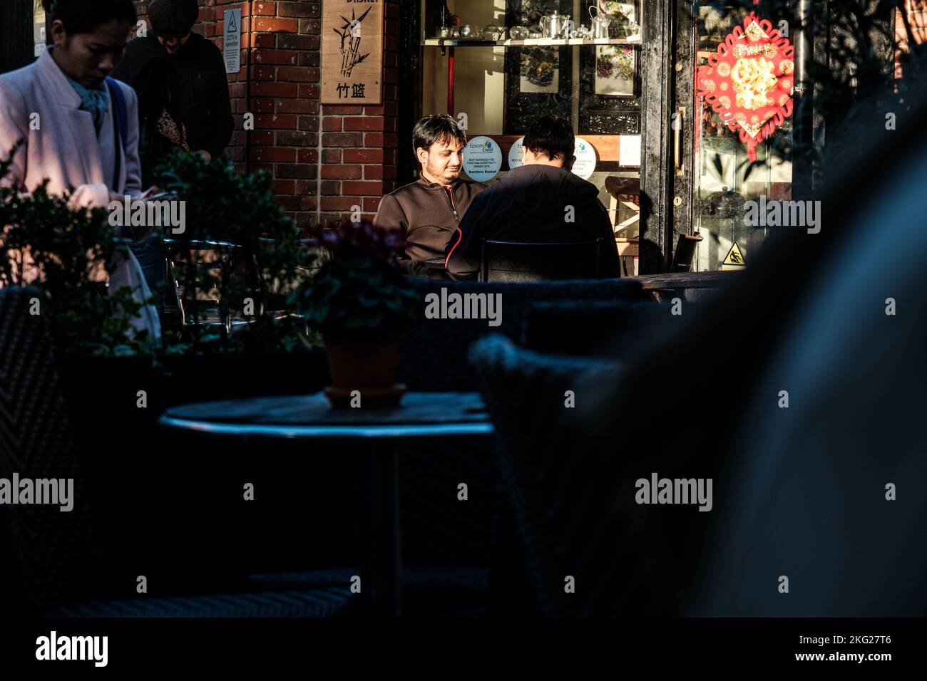 Epsom, Surrey, London, Großbritannien, 19 2022. November, zwei Männer sitzen vor Einem Restaurant, essen und unterhalten sich in der Abendsonne mit vorbeiziehenden Menschen Stockfoto