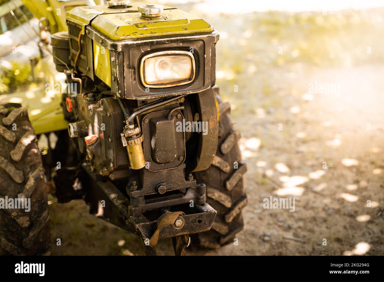Handlicher Traktor mit Scheinwerfernahaufnahme auf unscharfem Hintergrund. Mini-Traktor für landwirtschaftliche Zwecke Stockfoto