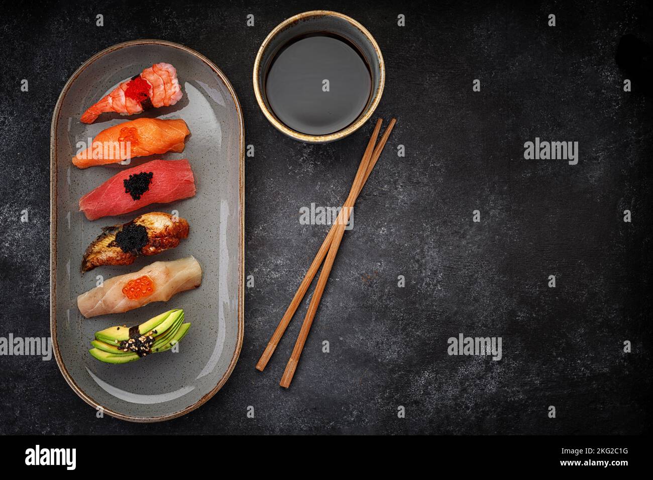 Verschiedene Nigiri Sushi auf einem Teller, auf dunklem Beton. Draufsicht Stockfoto