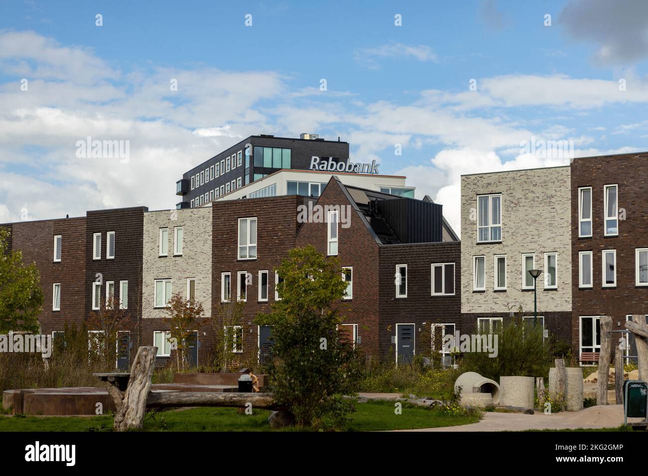 Eine Reihe von modernen Häusern, die sich über der niederländischen Bauernbank Rabobank erheben, vor einem blauen Himmel mit niedrigen Wolken und einem Spielplatz in der Nachbarschaft Stockfoto