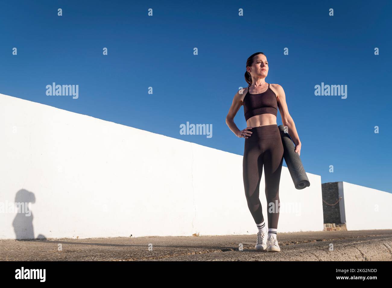 Sportliche Frau mit aufgerollter Trainingsmatte im Freien. Stockfoto