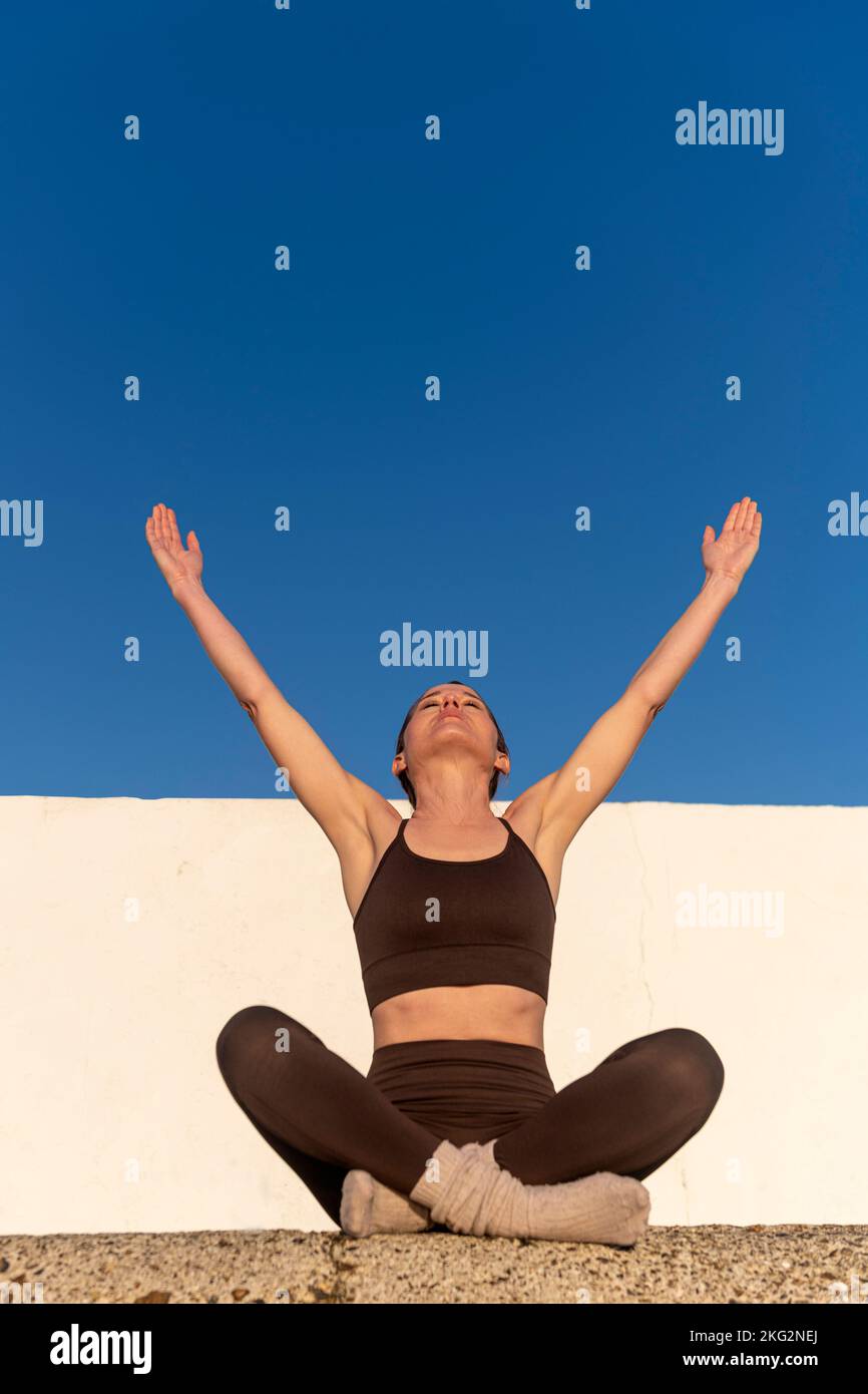 Sportliche Frau mit erhobenen Armen in den Himmel, genießen die Freiheit der Natur und Sonnenschein. Konzept von Wohlbefinden und gesunder Lebensweise Stockfoto