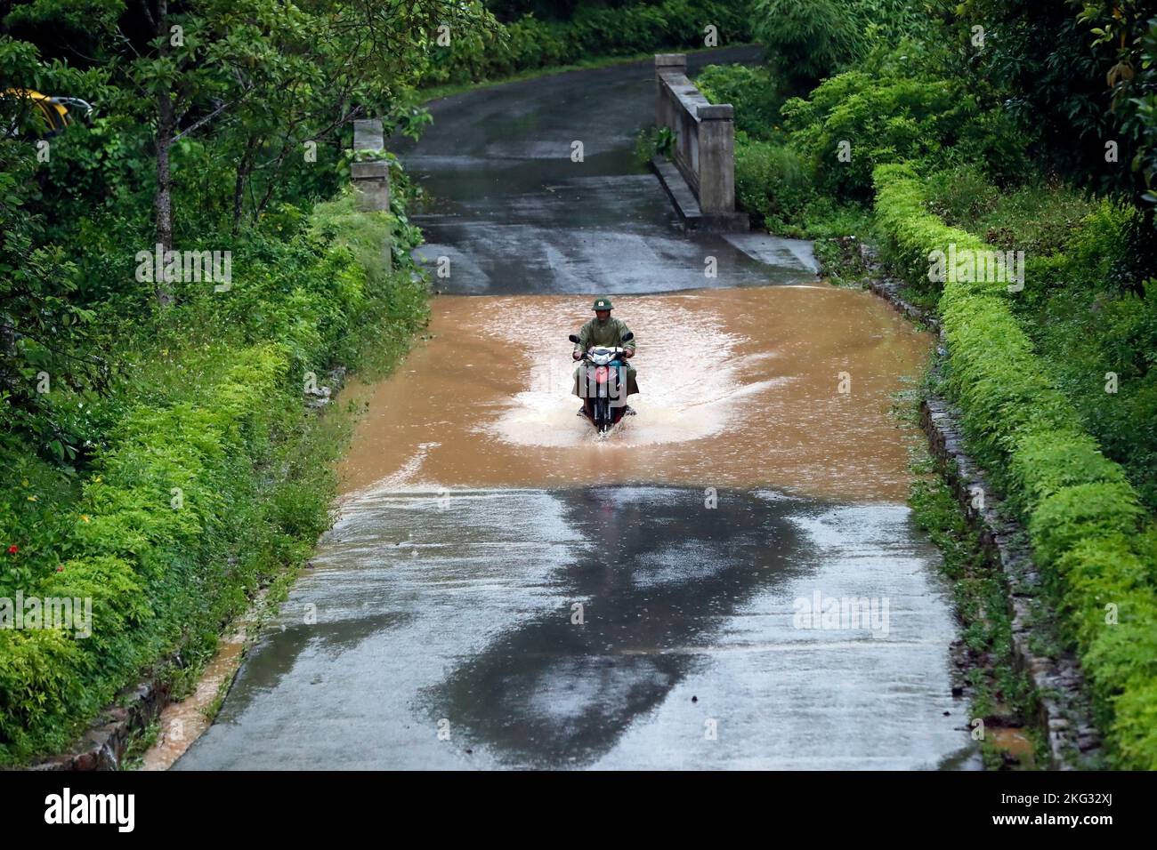 Während der Regenzeit fährt ein Mann mit dem Motorrad durch einen überfluteten Straßenabschnitt. Vietnam. Uong Bi. Vietnam. Stockfoto