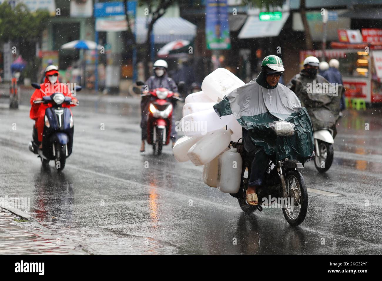 Vietnamesen mit Helm und Regenmantel fahren bei starkem Regen Motorrad, Wasser auf der Straße. Regenzeit in Saigon, Ho-Chi-Minh-Stadt. Vietnam. Stockfoto