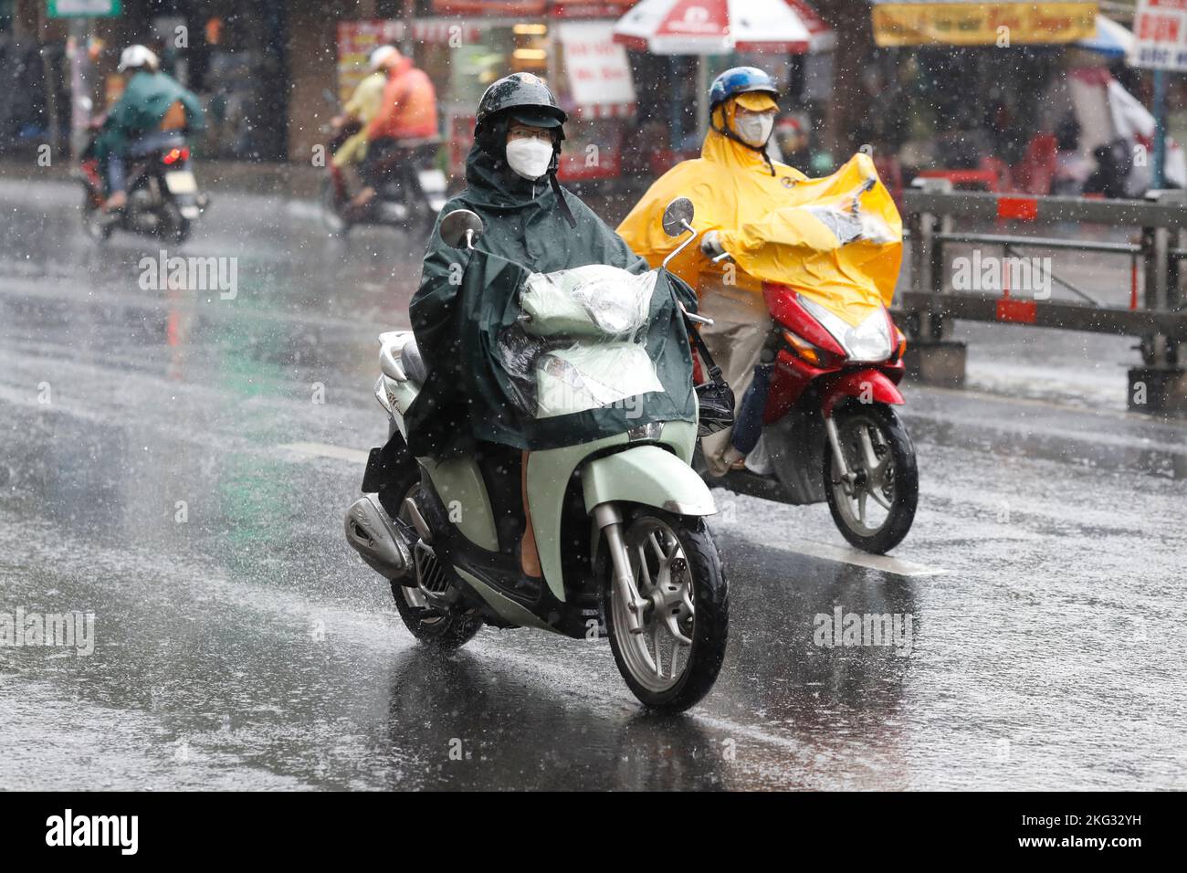 Vietnamesen mit Helm und Regenmantel fahren bei starkem Regen Motorrad, Wasser auf der Straße. Regenzeit in Saigon, Ho-Chi-Minh-Stadt. Vietnam. Stockfoto