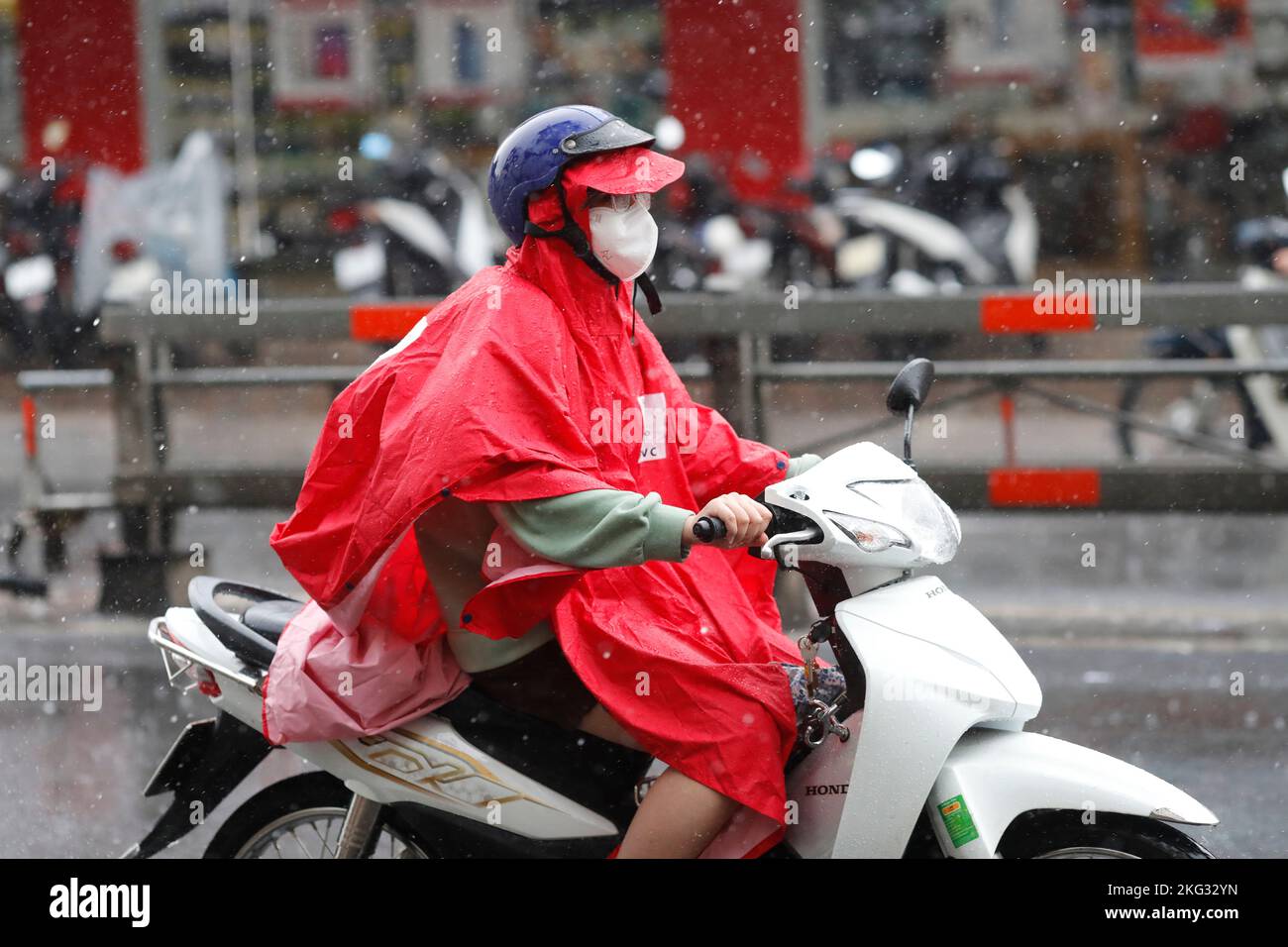 Frau mit Helm und Regenmantel fahren Motorrad bei starkem Regen, Wasser auf der Straße. Regenzeit in Saigon, Ho-Chi-Minh-Stadt. Vietnam. Stockfoto