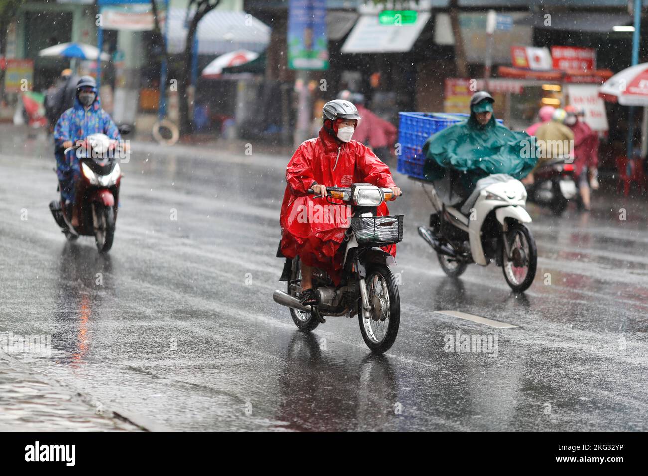 Vietnamesen mit Helm und Regenmantel fahren bei starkem Regen Motorrad, Wasser auf der Straße. Regenzeit in Saigon, Ho-Chi-Minh-Stadt. Vietnam. Stockfoto
