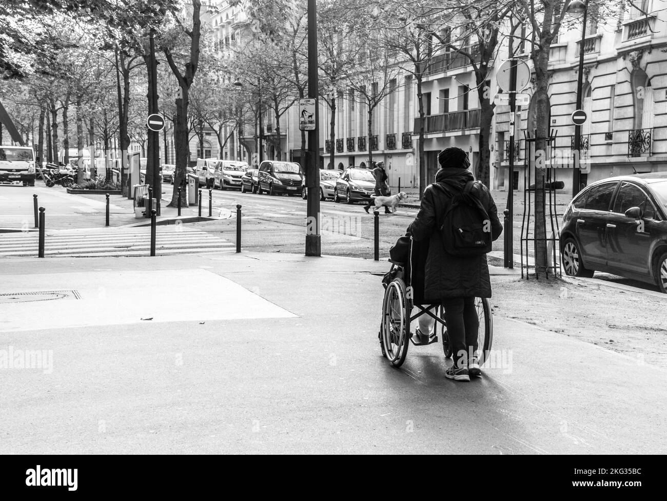 Eine Graustufenaufnahme einer Frau, die eine Person in einem Rollstuhl auf den Straßen von Paris, Frankreich, schiebt. Stockfoto