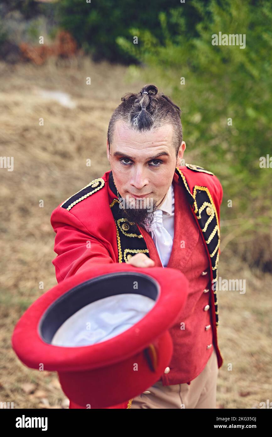 Hoher Winkel des Mannes in schickes rotes Anzug zeigt Hut und Blick auf die Kamera während der Performance im Park Stockfoto