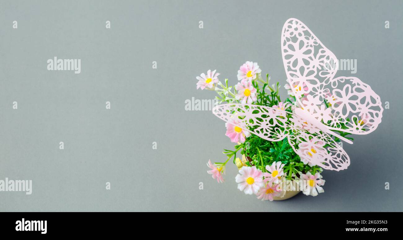 Schmetterling aus Papier auf pinkfarbenem Blumentopf auf grauem Hintergrund mit leerem Platz. Stockfoto