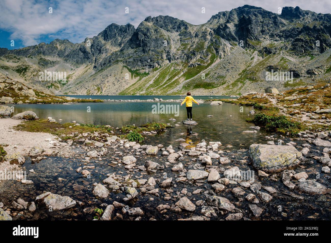 Wanderer Frau erkunden Sie die fantastische Landschaft und genießen Sie die Aussicht in der Nähe eines Bergsees in gelb in Jacke, hohe Tatra, Slowakei Stockfoto