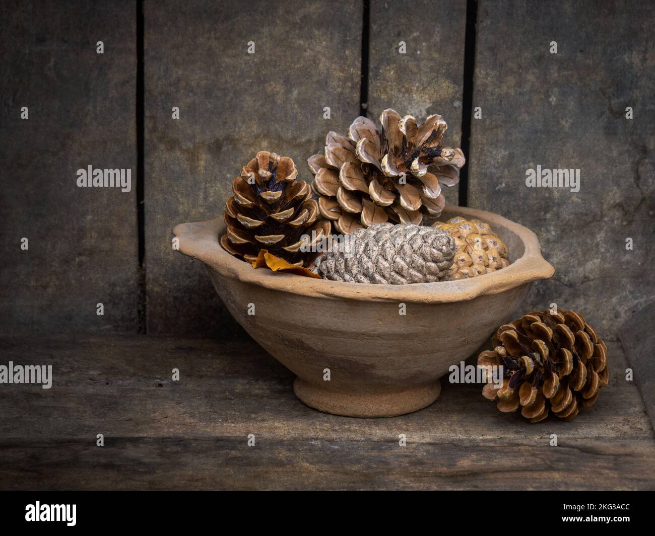 Eine alte, Töpferschale voller Kiefernzapfen in einer Holzkiste. Rustikal. Stockfoto