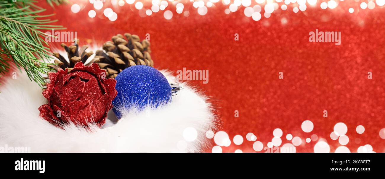 Weihnachtskugeln mit Zapfen in Pelz-Geschenktüte mit Tannenzweig auf rot verschwommenem Hintergrund mit weißem Bokeh. Banner, Konzept des Einkaufs, Verkauf. Neujahr. C Stockfoto