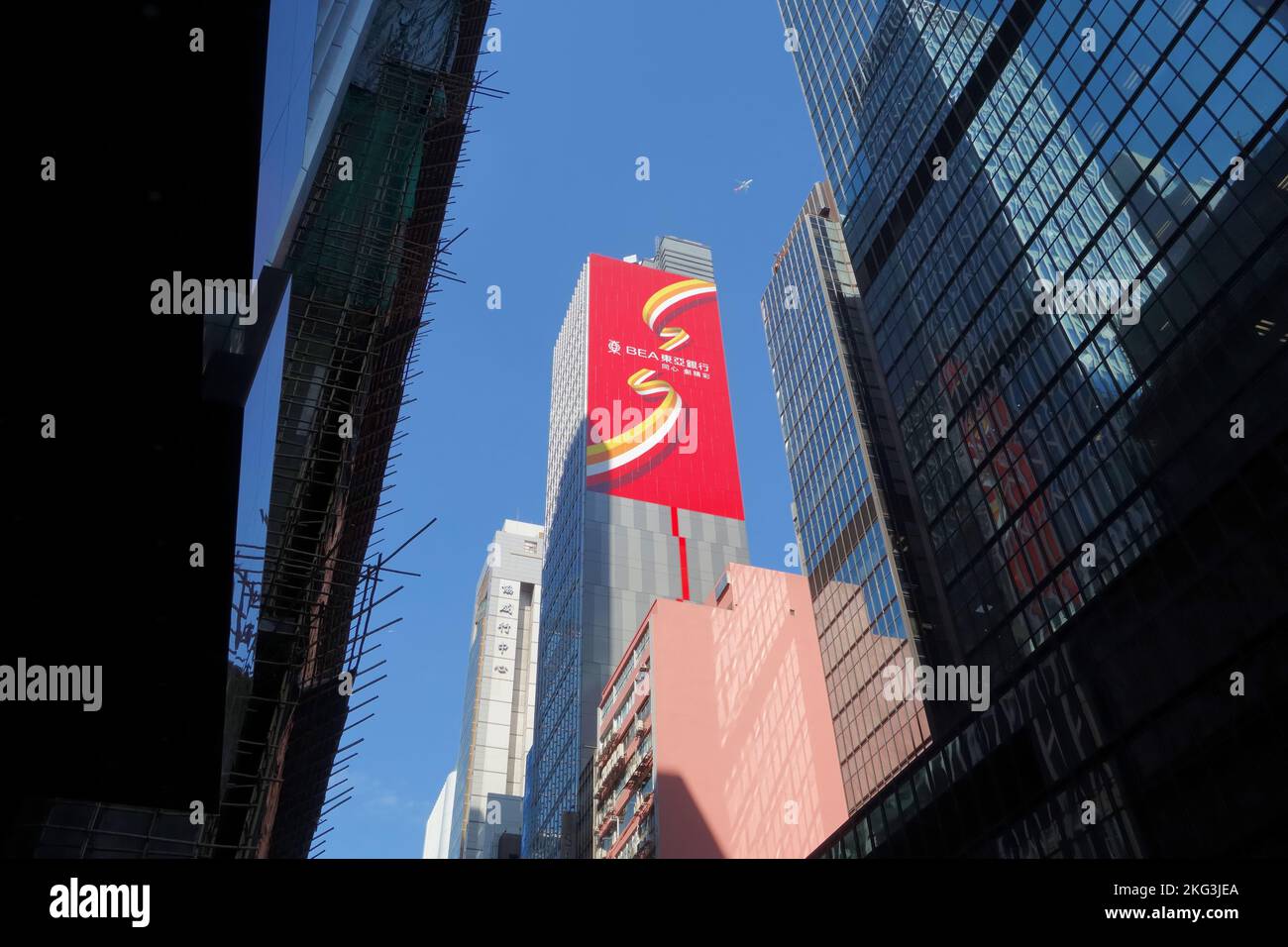 Aus der dunklen Straße ragt das Gebäude der Bank of Ostasien (BEA) in den Sonnenschein Hongkongs, der fast das Flugzeug darüber berührt Stockfoto