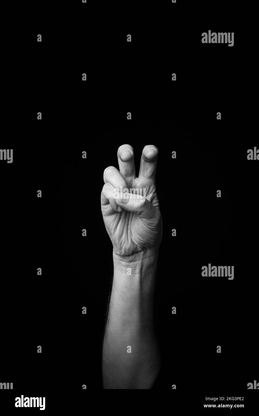 Dramatisches Schwarzweißbild eines männlichen Hands, der den Buchstaben „X“ in der Zeichensprache Fench schreibt, isoliert vor einem dunklen Hintergrund mit Kopierraum Stockfoto