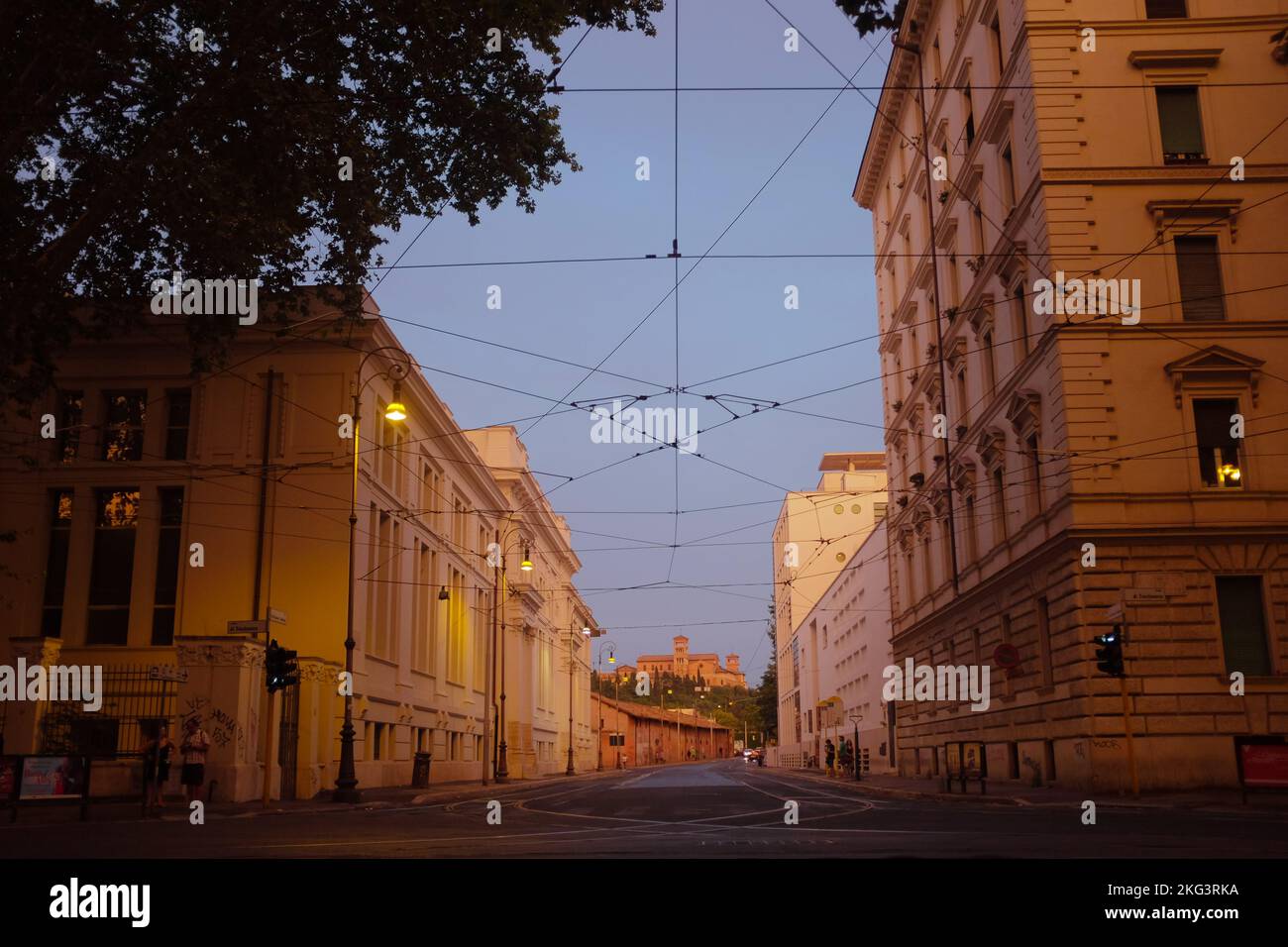 Leere Straße in Rom, Italien bei Sonnenuntergang. Postkarte der romantischen Ewigen Stadt zur goldenen Stunde. Gebäude in warmem Licht, Himmelblau, Drähte bilden ein Netz. Stockfoto