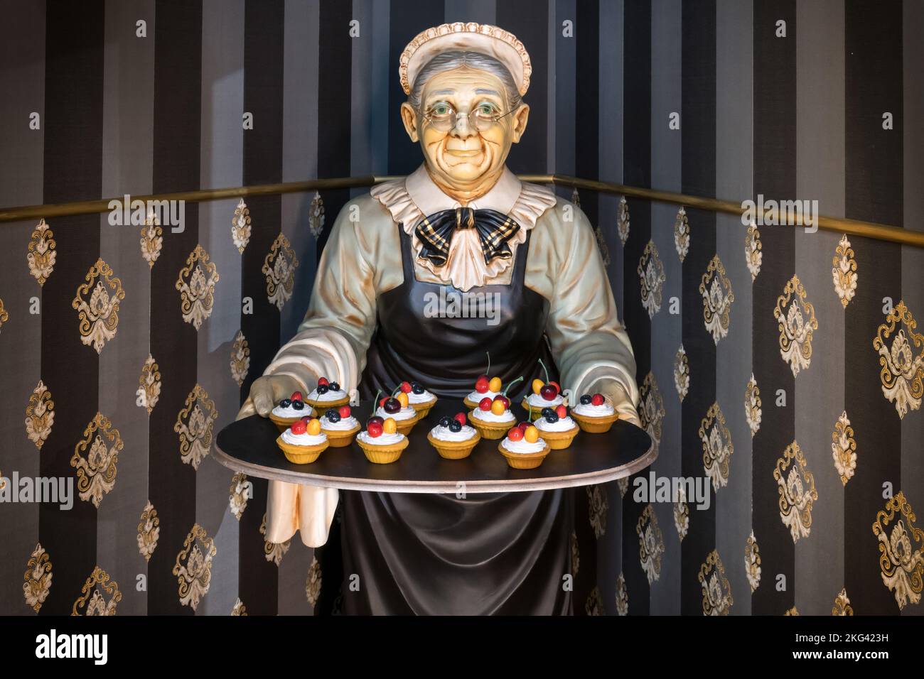 Statue der Großmutter, die Tablett mit kleinen Törtchen in der Ecke der gestreiften Wände im Restaurant trägt Stockfoto