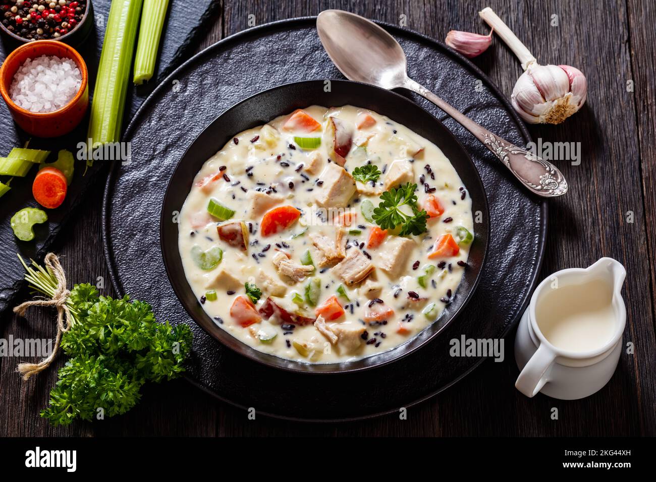 PutenwildReissuppe mit roten Kartoffeln. Karotten, Sellerie, Gewürze und Kräuter in schwarzer Schale auf dunklem Holztisch mit Zutaten Stockfoto