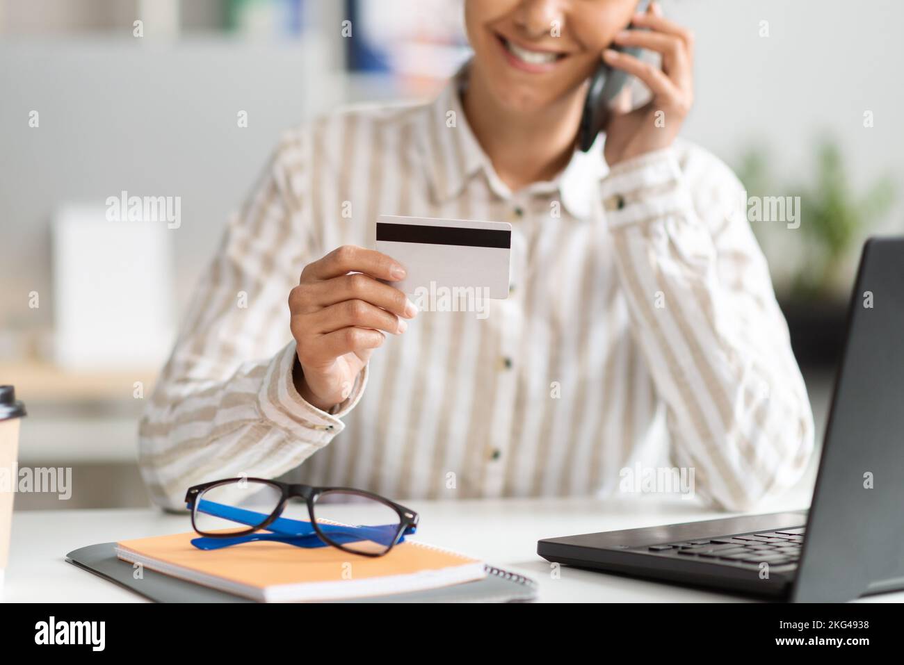 Unbekannte Geschäftsfrau mit Kreditkarte, die bei der Bank anruft, während sie im Büro sitzt Stockfoto