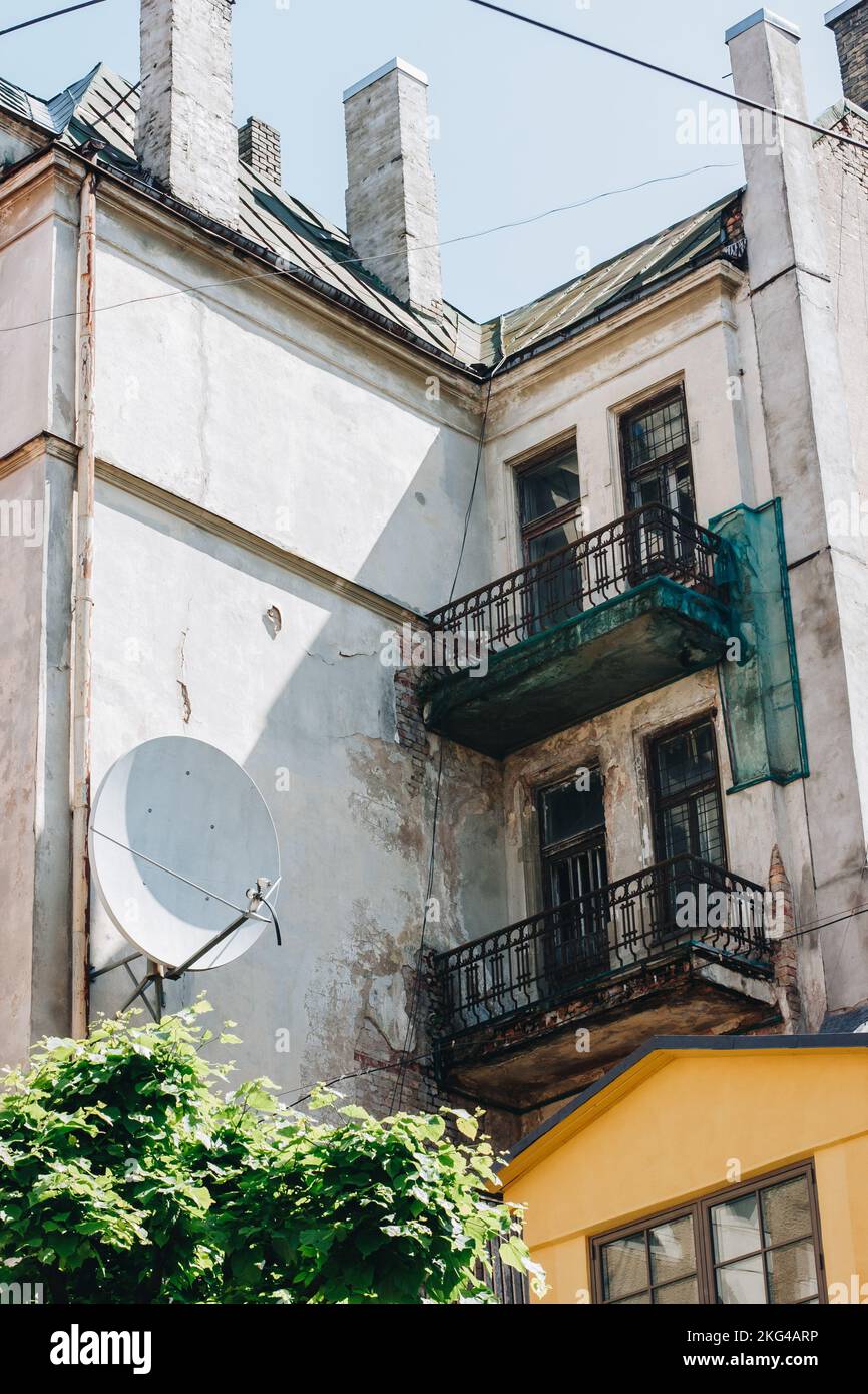 Weißes Wohnhaus mit Balkonen, umgeben von Metallzäunen und einer riesigen Satellitenschüssel an der Wand. Stockfoto