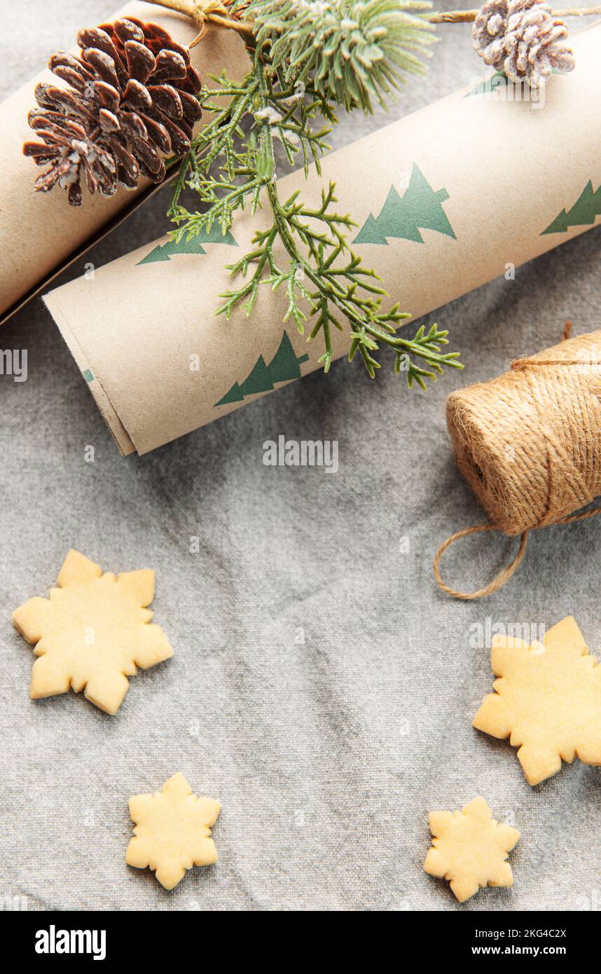 Geschenkpapier mit einem Kiefernzweig und Weihnachtskekse auf einem textilen Hintergrund. Das Konzept der Vorbereitung auf die Weihnachtsfeiertage. Flach liegend. Kopie sp Stockfoto