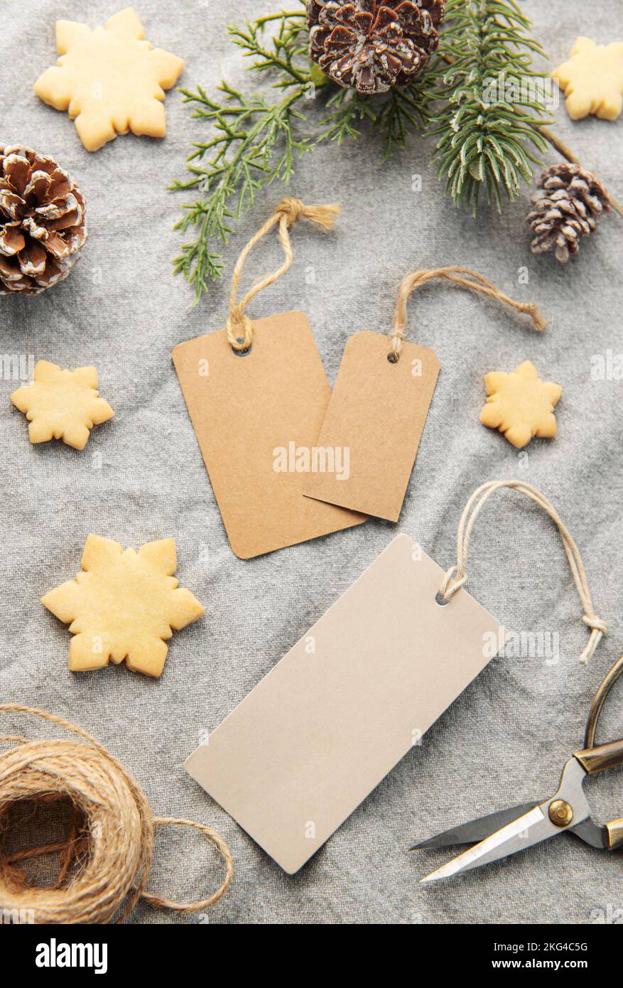 Leere Geschenkanhänger mit Tannenzweig und Weihnachtskeksen auf textilen Hintergrund. Das Konzept der Vorbereitung auf die Weihnachtsfeiertage. Flach liegend Stockfoto