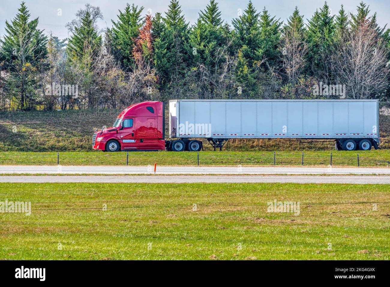 Horizontale Aufnahme eines roten Traktorfahrers auf einer einsamen Spätsommerstraße. Stockfoto