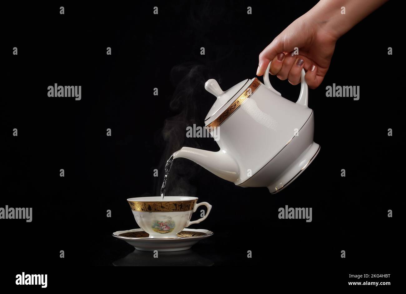 Gießen Sie eine weiße Teetasse mit einer Teekanne auf schwarzem Hintergrund ein Stockfoto