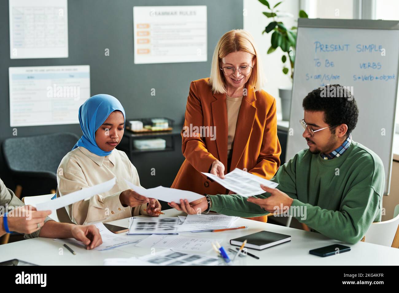 Eine Gruppe interkultureller Schüler, die Grammatiktests machen, während der Lehrer ihnen während des Unterrichts der englischen Sprache Papiere übergibt Stockfoto
