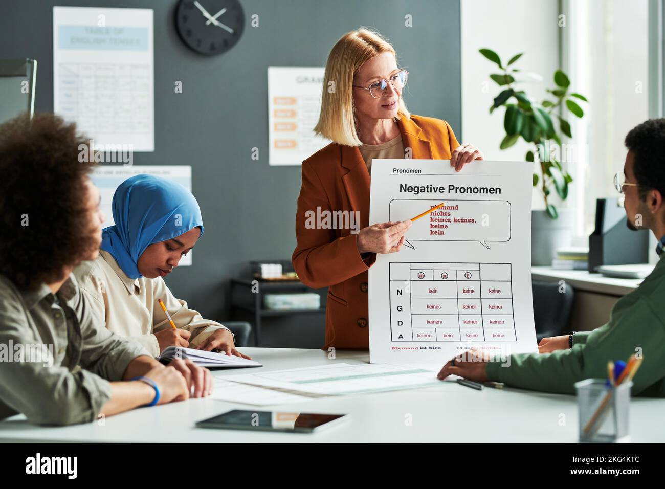 Selbstbewusster Lehrer der deutschen Sprache, der der Gruppe von Schülern negative Pronomen erklärt, während er während der Präsentation auf den Tisch zeigt Stockfoto