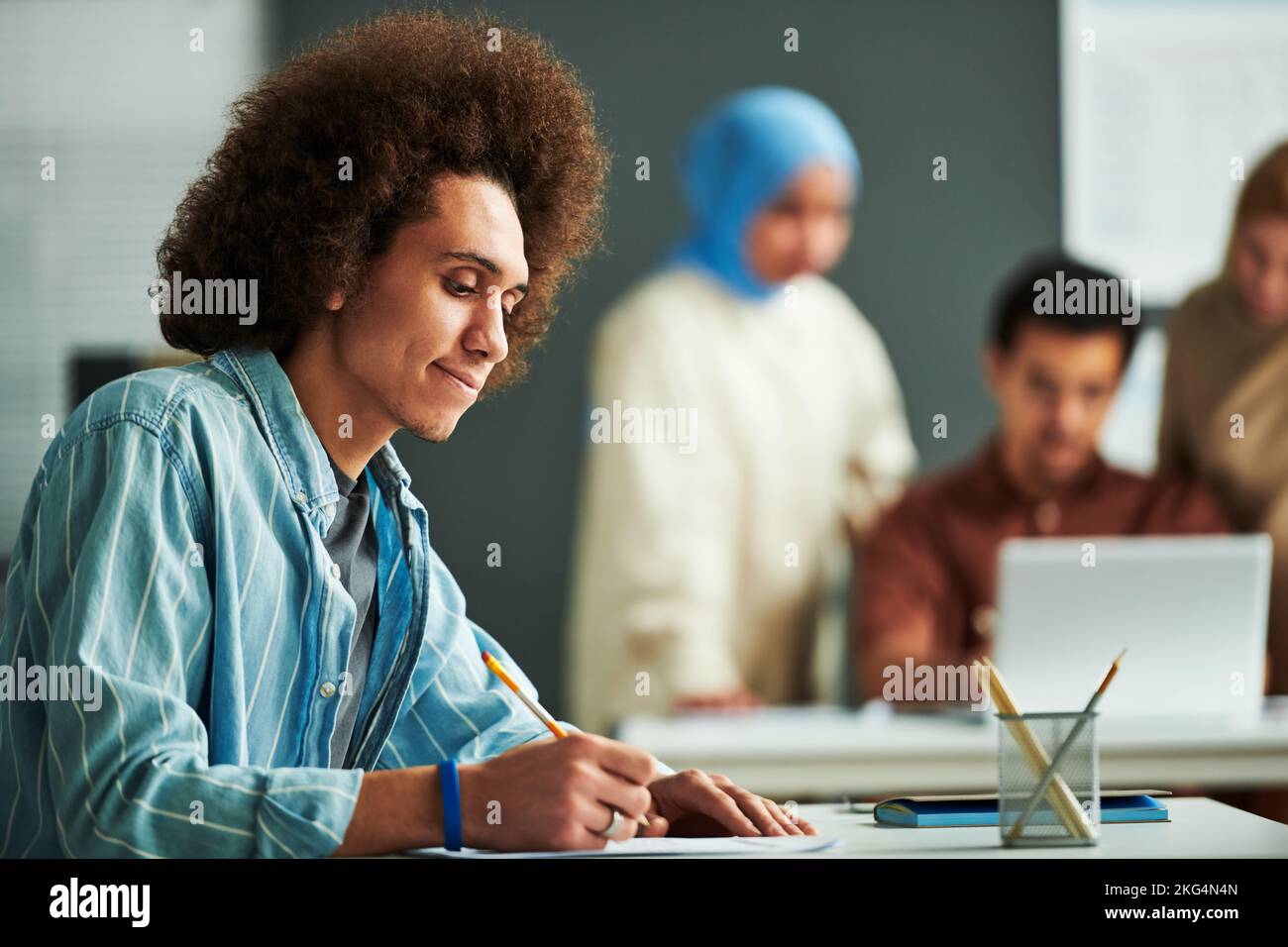 Seitenansicht eines jungen multiethnischen Studenten, der Papier mit Grammatiktest betrachtet und darauf zeigt, während er an die richtige Antwort im Unterricht denkt Stockfoto