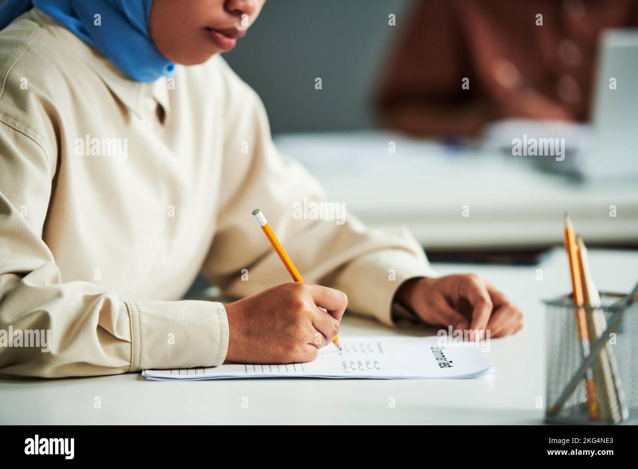 Hand einer jungen muslimischen Studentin mit Bleistift über Papier mit Grammatiktest, der richtige Antworten während der individuellen Arbeit tickt Stockfoto