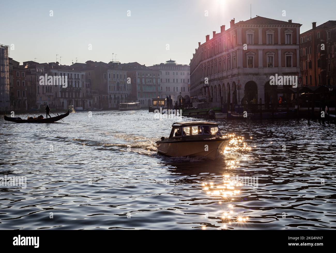 Am frühen Morgen scheint Licht durch den Canale Grande, Venedig. Ein kleines privates Motorboot fährt in Richtung Kamera und eine Gondel überquert den Kanal Stockfoto