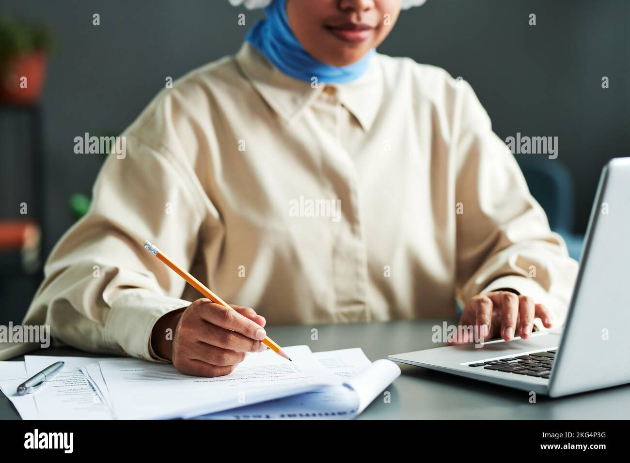 Selektiver Fokus auf die Hand eines jungen Studenten mit Bleistift über Papier mit Grammatiktest, der während des Online-Unterrichts vor dem Laptop sitzt Stockfoto