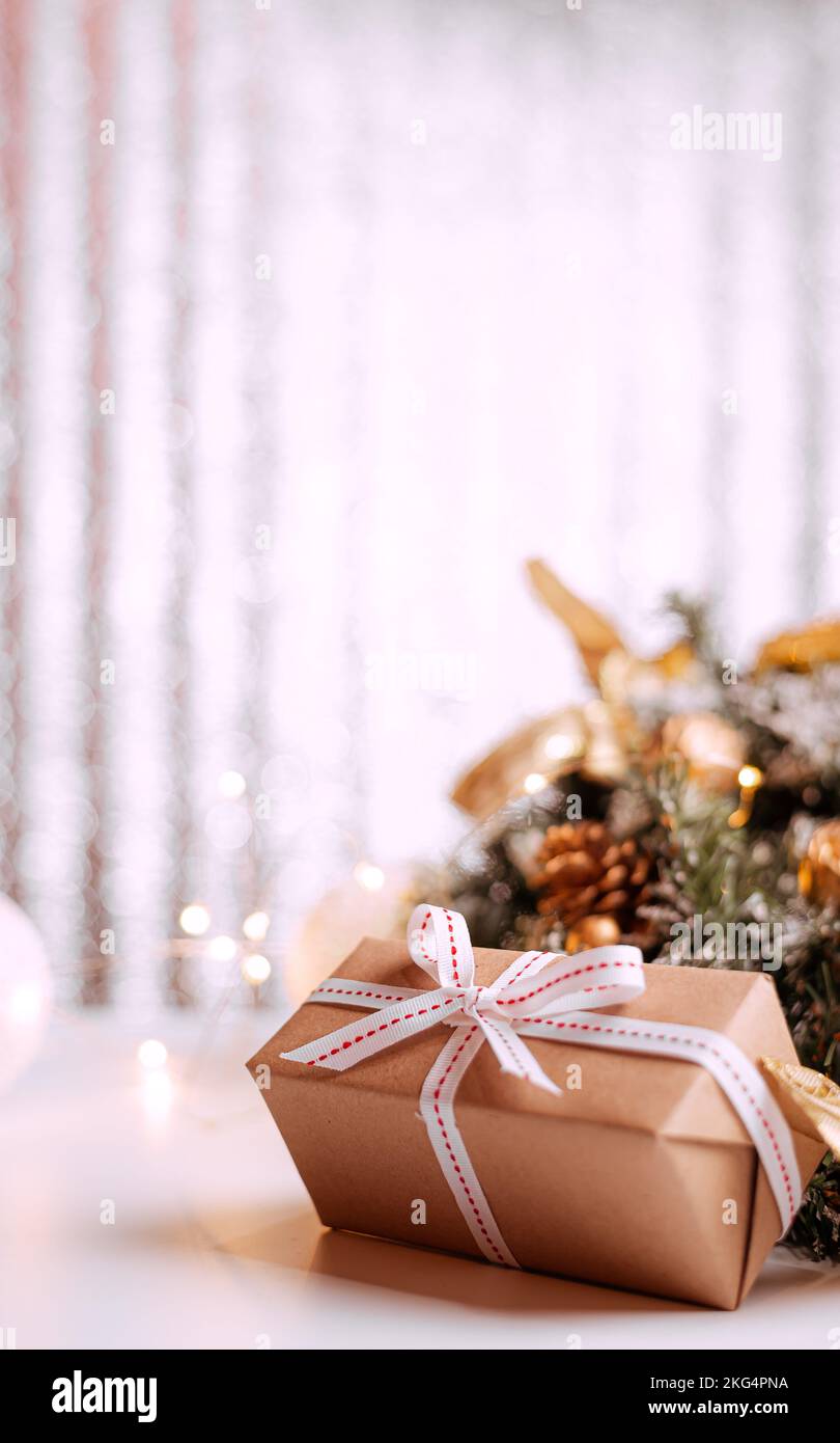 Geschenkbox aus Kraftkarton mit rauem Juteseil auf grauem Holzhintergrund mit Zweigen von Weihnachtsbäumen und Weihnachtsdekorationen Stockfoto
